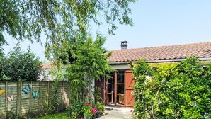 Et hus med tegltag, træhegn og en have med forskellige planter og blomster.