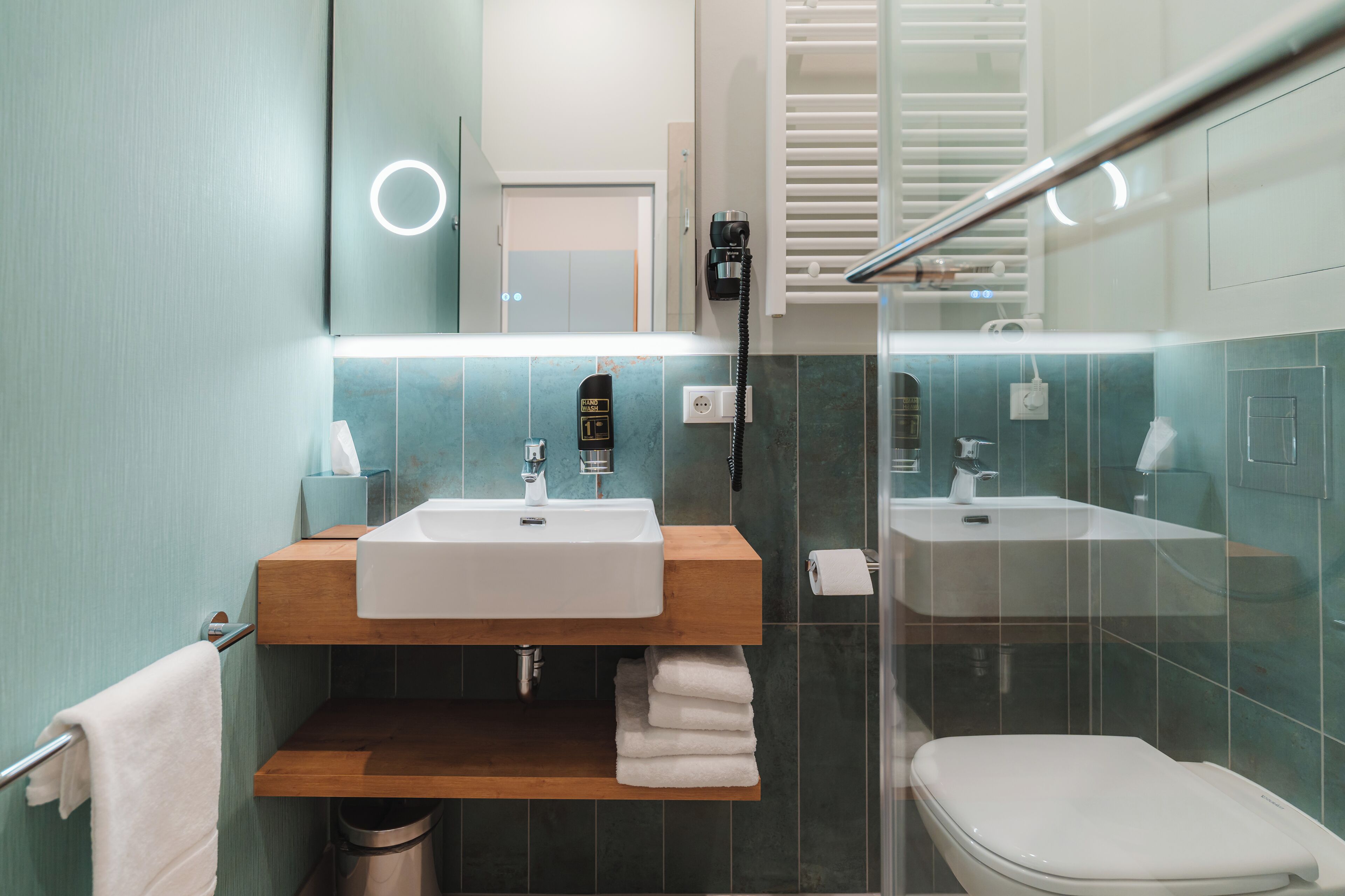 Un bagno moderno con un mobile lavabo in legno, due lavandini, un WC e un box doccia in vetro.