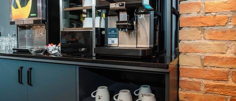 Una estación de café con una máquina de café con el logo de la marca, un molinillo de café y una exhibición de tazas con el logo.