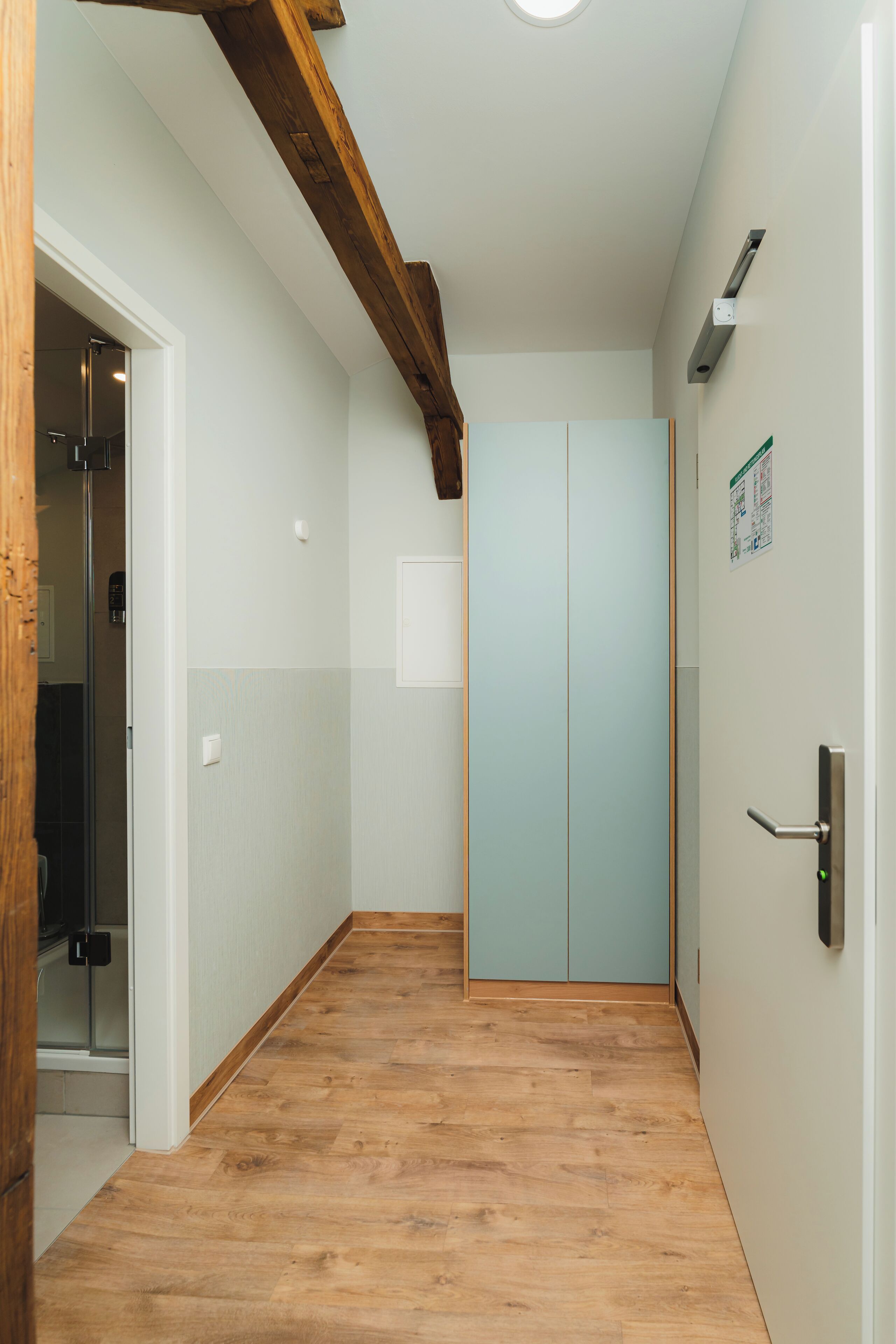 A hallway with wooden flooring, a wooden ceiling beam, and a light blue door.