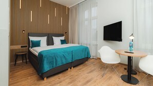 A modern hotel room with a bed, a TV, a small table, and a chair.