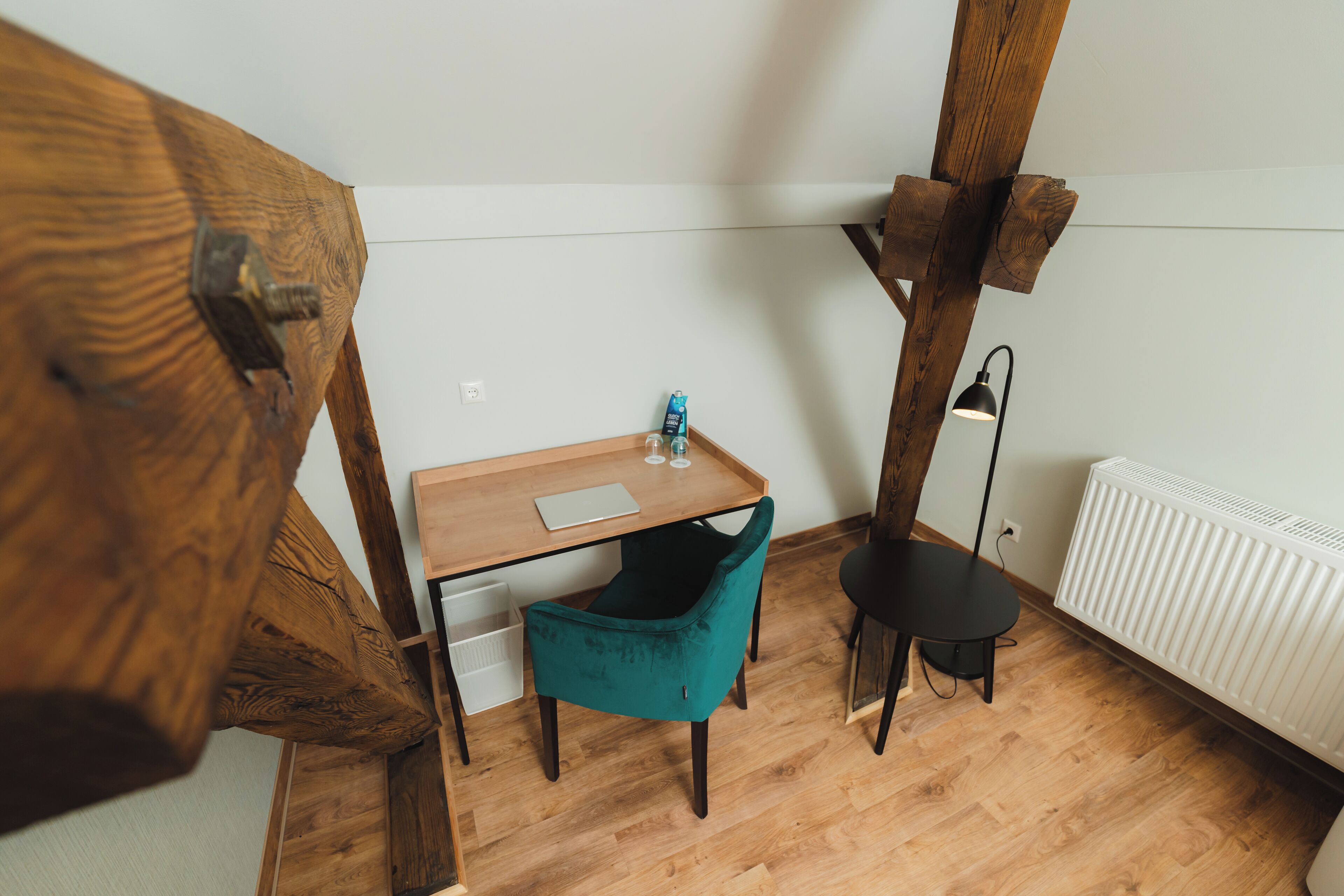 A corner room with a wooden desk, teal chair, and a black floor lamp.
