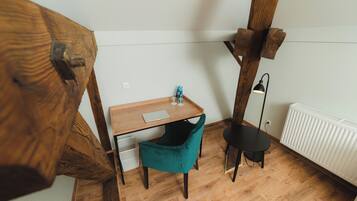 A corner room with a wooden desk, teal chair, and a black floor lamp.