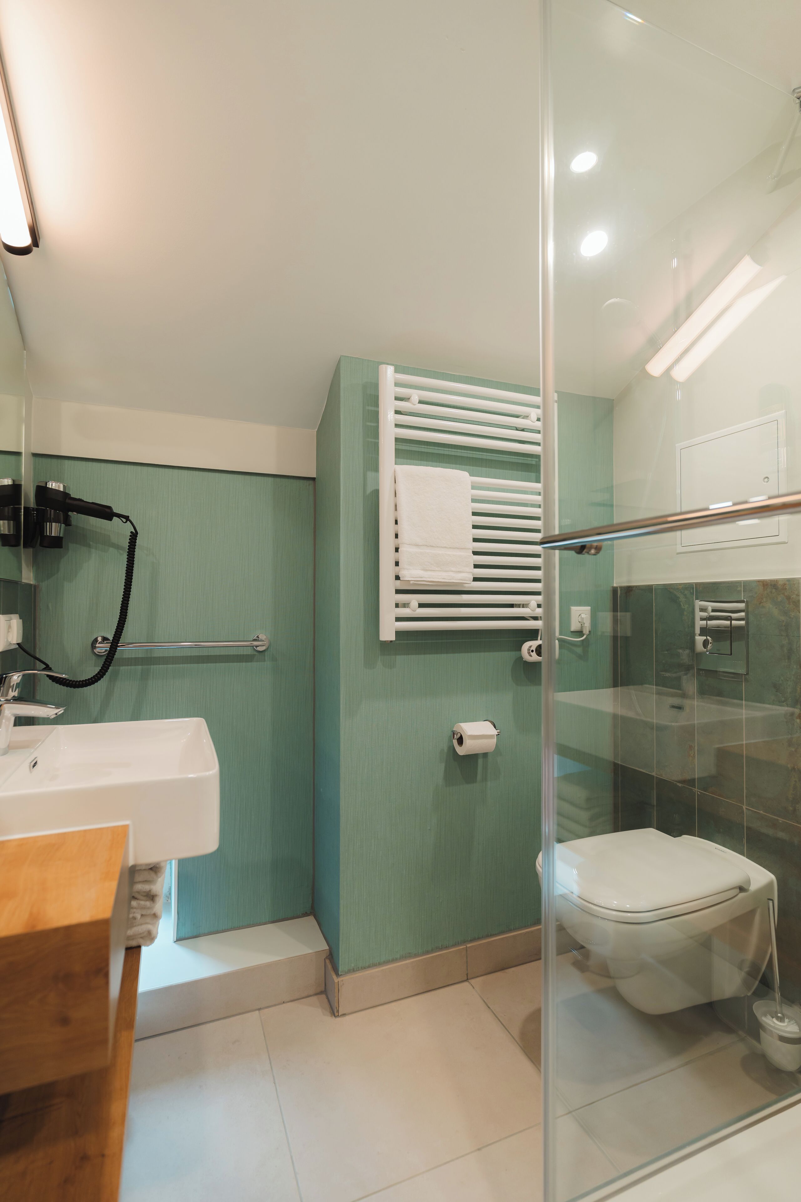 A modern bathroom with a glass shower enclosure, a white sink, and a towel rack.