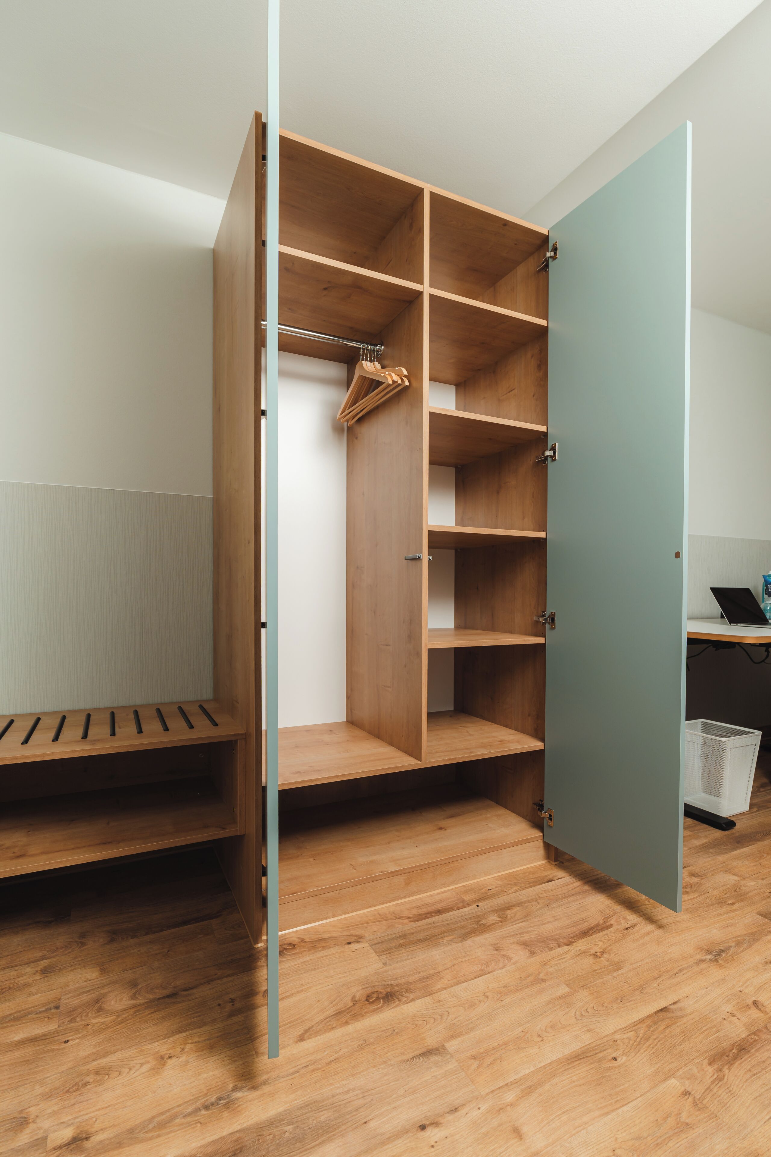 Un vestidor amplio con puertas abiertas, estantes de madera y un banco.