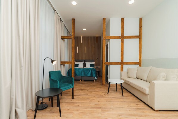 Une chambre d’hôtel moderne avec un plancher en bois, un lit avec une literie de couleur turquoise, un canapé blanc, un fauteuil turquoise et une petite table noire.
