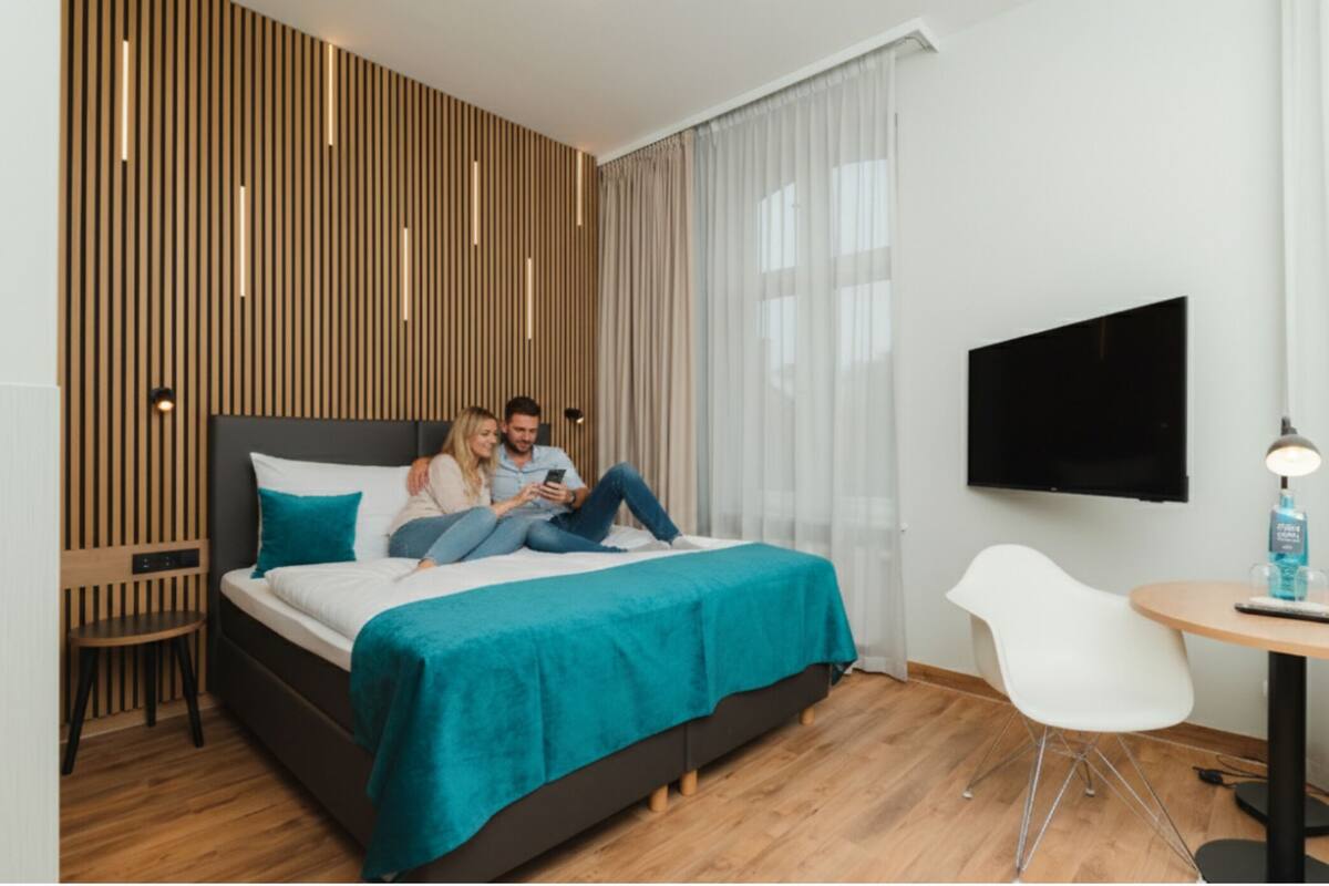 Ein modernes Hotelzimmer mit Bett, Fernseher, Schreibtisch und Stuhl.