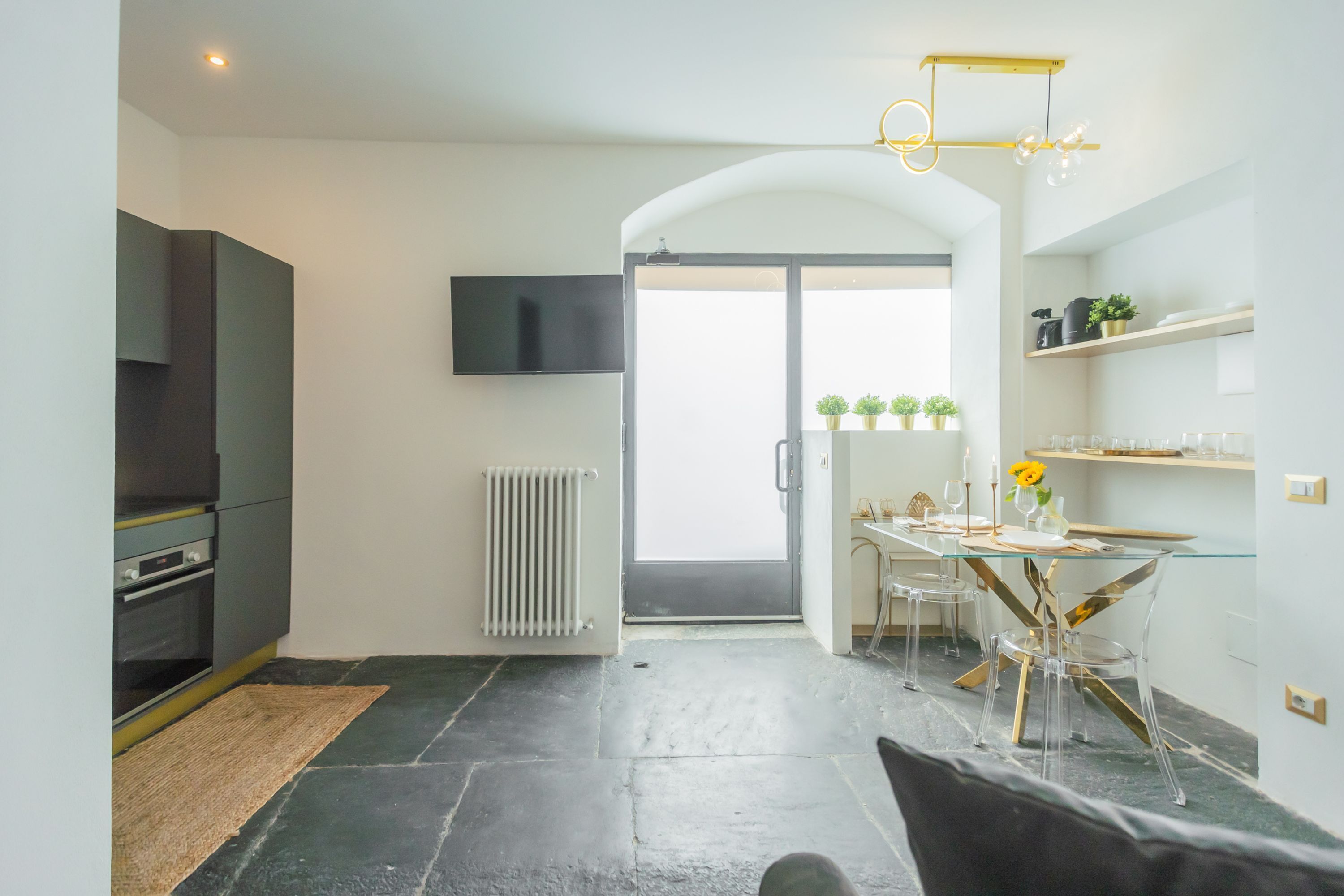 Eine moderne Küche mit Einbauofen, ein Essbereich mit Glastisch und Stühlen sowie ein an der Wand montierter Fernseher.