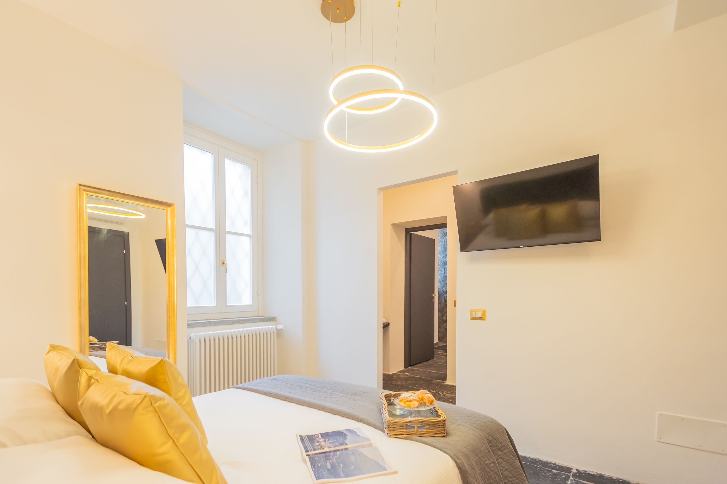 Une chambre d’hôtel moderne équipée d’un lit, d’une télévision, d’une fenêtre et d’une porte donnant sur une autre pièce.