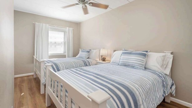 A bedroom with two beds, a ceiling fan, a window with curtains, and a bedside lamp.