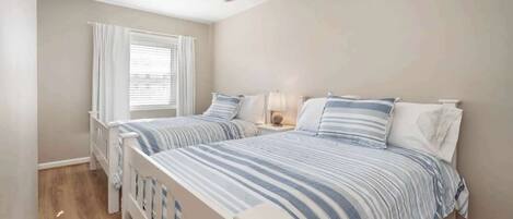 A bedroom with two beds, a ceiling fan, a window with curtains, and a bedside lamp.