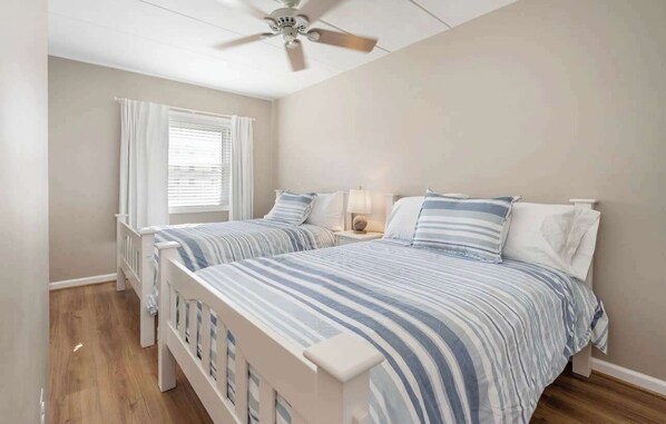 Une chambre avec deux lits, un ventilateur de plafond, une fenêtre avec des rideaux et une lampe de chevet.
