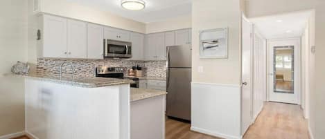 A modern kitchen with white cabinetry, a central island, a stainless steel refrigerator, and a microwave.