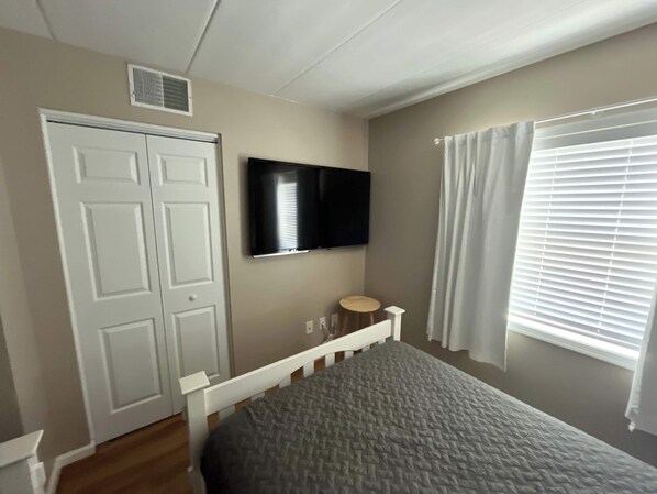 A bedroom with a bed, a television mounted on the wall, a door, and a window with blinds.