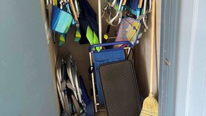 A storage area with various cleaning tools and equipment, including brooms, mops, and a dustpan.