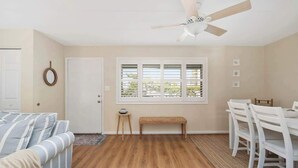 A room with a ceiling fan, a window with blinds, a bench, a dining table with chairs, and a door. - Ocean Block-Uptown -Northside Park-Sleeps 6 (Ocean City)