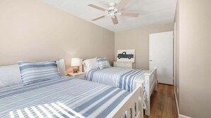 A bedroom with two beds, a ceiling fan, a nightstand with a lamp, and a door leading to another room. - Ocean Block-Uptown -Northside Park-Sleeps 6 (Ocean City)