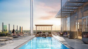 Une piscine sur le toit, dotée de chaises longues et d’un espace salon couvert, offrant une vue sur la ville.