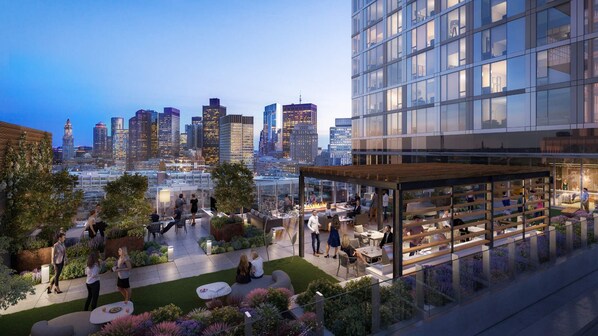 Un jardin sur le toit, aménagé avec des espaces de détente, un bar et offrant une vue sur les toits de la ville au crépuscule.