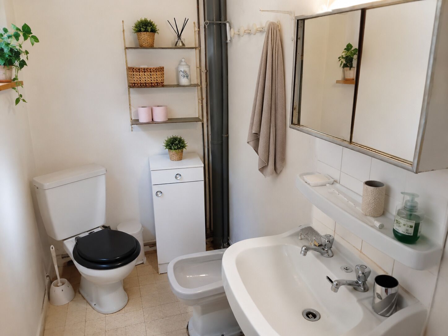 Baño con inodoro, bidé, lavamanos y repisas con artículos de aseo.