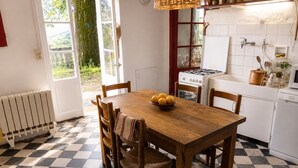 A kitchen with a checkered floor, wooden table, chairs, a stove, and a window with a view of greenery. - Cévennes-style house surrounded by nature with a swimming pond (Monoblet)