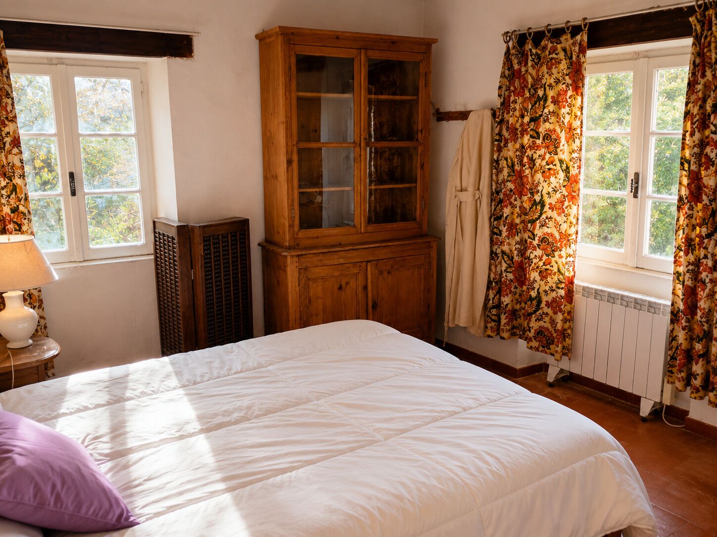Une chambre à coucher avec un lit, une armoire en bois, un radiateur et des rideaux à motifs floraux.