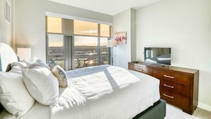 Une chambre avec un grand lit, une télévision, une commode et une fenêtre donnant sur la ville.
