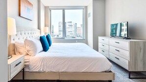 A modern hotel room with a large bed, a desk with a lamp, a dresser, and a TV. - Private Apt Downtown Walk to Harbor (Boston)