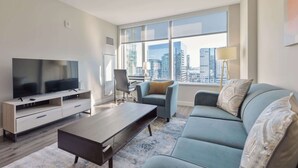 A modern living room with a large TV, a sofa, a coffee table, and a city view through large windows. - Private Apt Downtown Walk to Harbor (Boston)