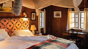 Una habitación con cama, escritorio y silla. Hay una ventana con cortinas y un cuadro en la pared.