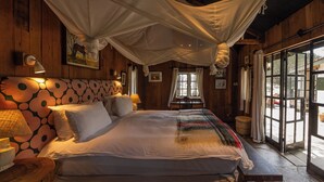 Una cama con dosel, paredes de madera, cabecera estampada y una ventana con cortinas.
