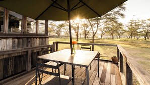 A wooden deck with a table and chairs, a potted plant, and a view of trees and a distant building. - Unique 2-story tower with 360° wildlife views and stargazing showers. (Naivasha)
