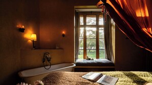 Et badeværelse med badekar, et vindue med gardiner og et natbord med lampe.