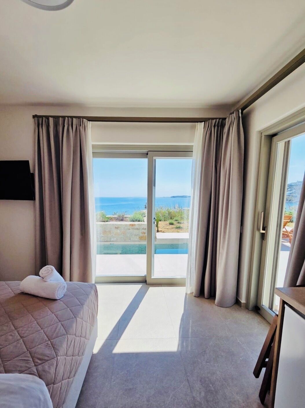 Habitación de hotel con cama, televisión y vista al mar a través de una puerta corrediza de vidrio.