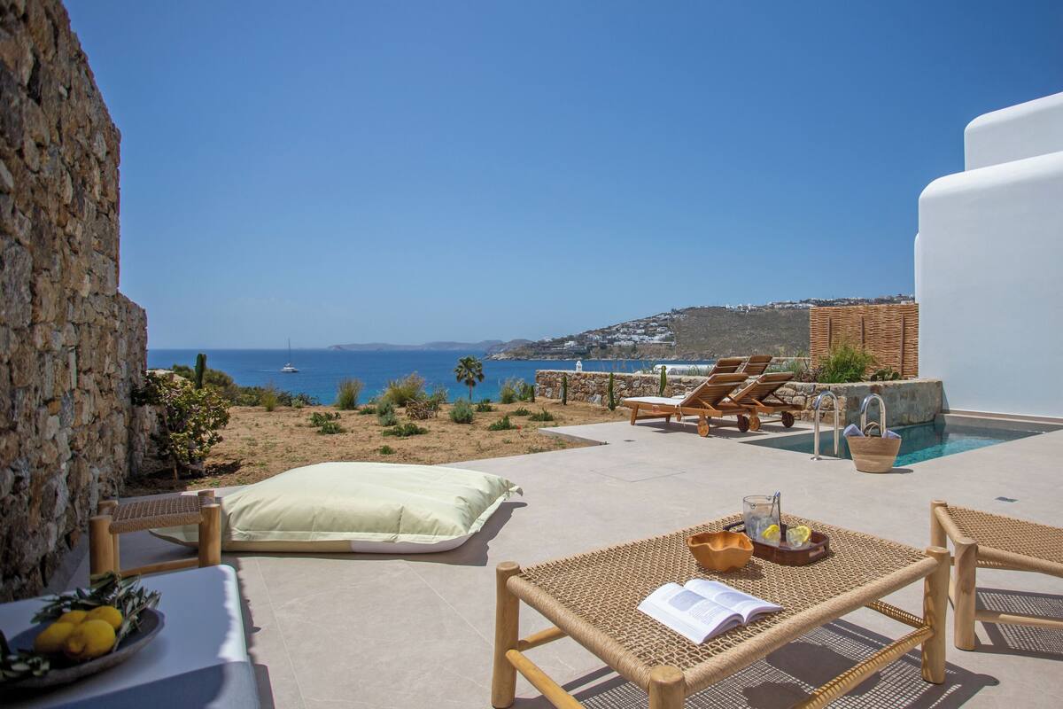 A terrace with wicker furniture, a pool, and a view of the sea and hills.