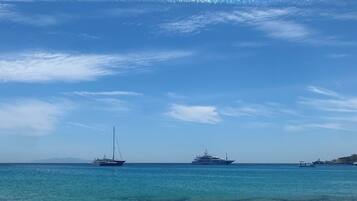 A beach with clear skies and calm waters. There are two boats visible in the distance.