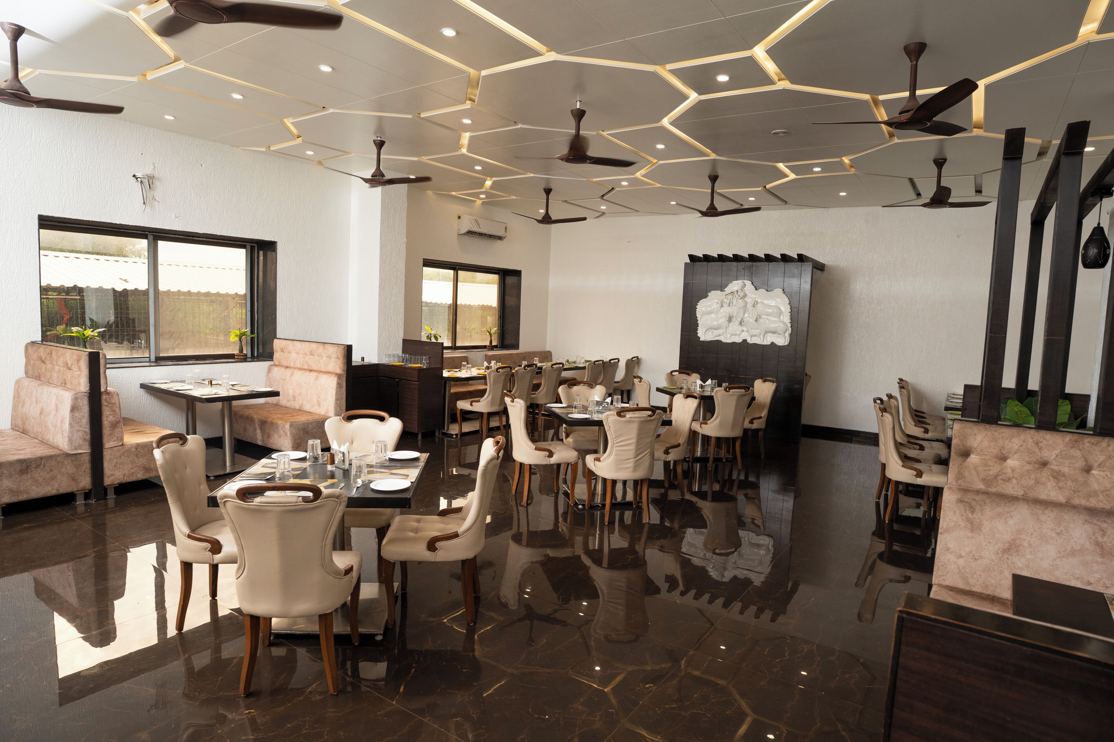 A modern dining area with multiple tables and chairs, ceiling fans, and a large window providing natural light.