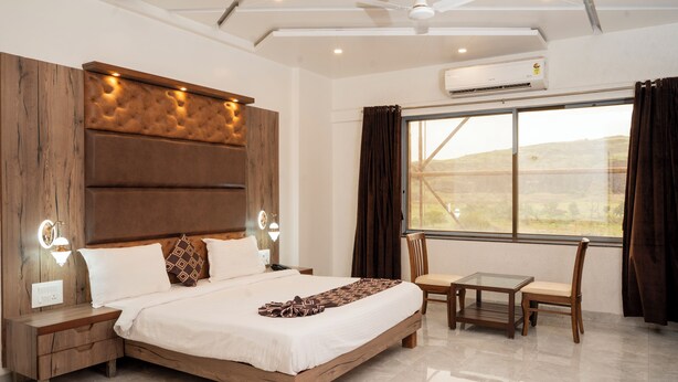 Une chambre d’hôtel moderne avec un grand lit, une petite table et des chaises, un ventilateur de plafond et une grande fenêtre avec des rideaux.