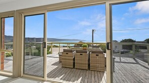 A balcony with a view of a beach and ocean, wicker furniture, and a wooden deck. - Majestic Views (Marengo)