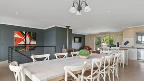 A modern kitchen with a central island, a dining area with a long table and chairs, and a staircase leading to an upper level.