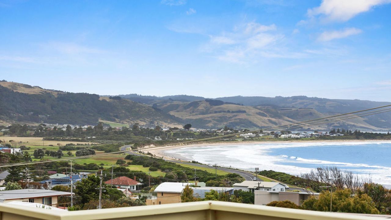 A coastal landscape with a beach, houses, and hills in the background.