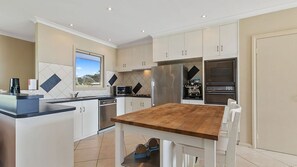 A modern kitchen with white cabinets, a wooden dining table, and built-in appliances.