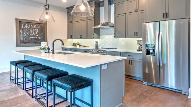Una cocina moderna con armarios grises, un refrigerador de acero inoxidable, una isla grande con taburetes de bar e iluminación colgante.