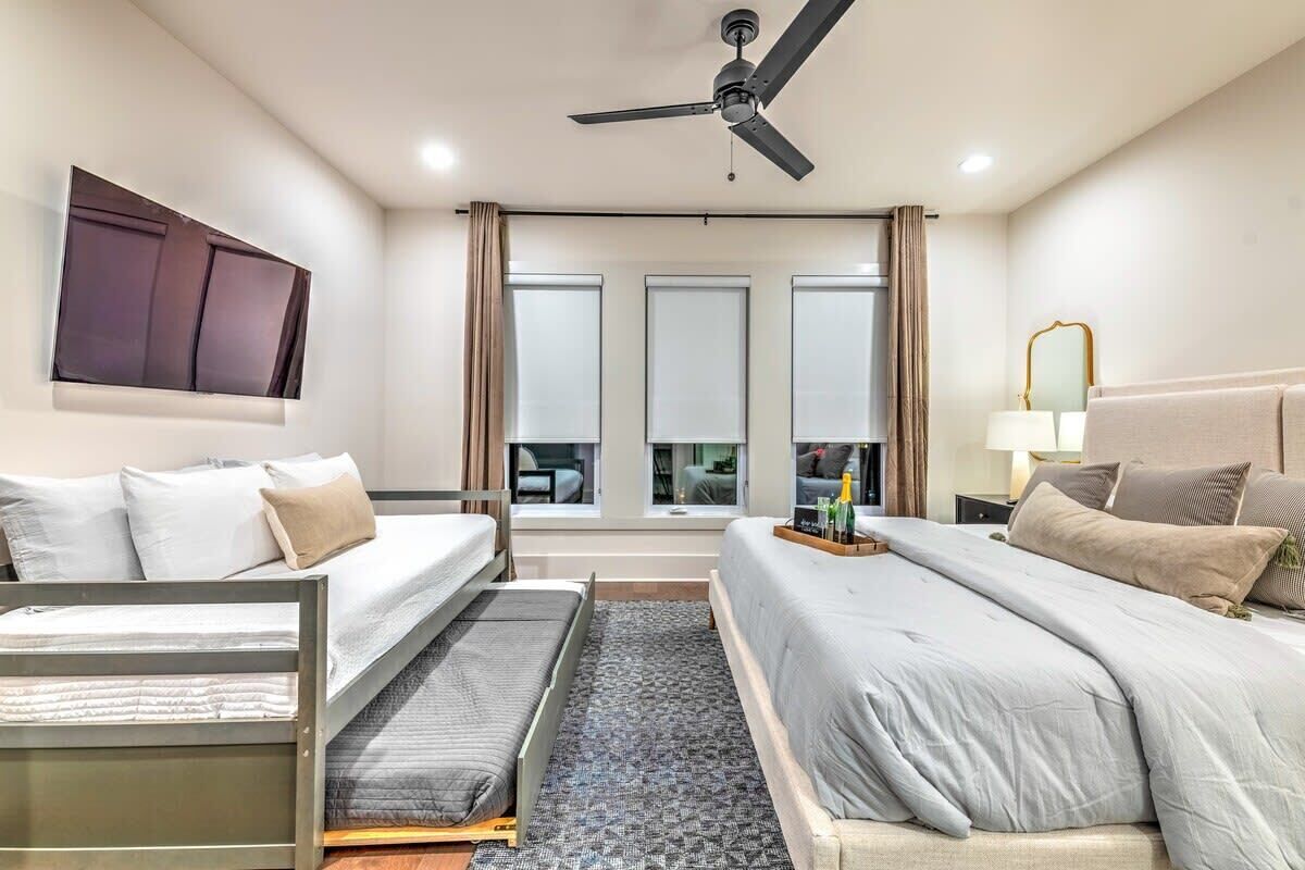 A modern hotel room with two beds, a ceiling fan, a large window with curtains, and a view of the city.