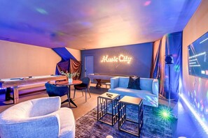 Une pièce équipée d’une table de billard, d’un canapé et d’un panneau lumineux au néon sur lequel on peut lire « Music City ».