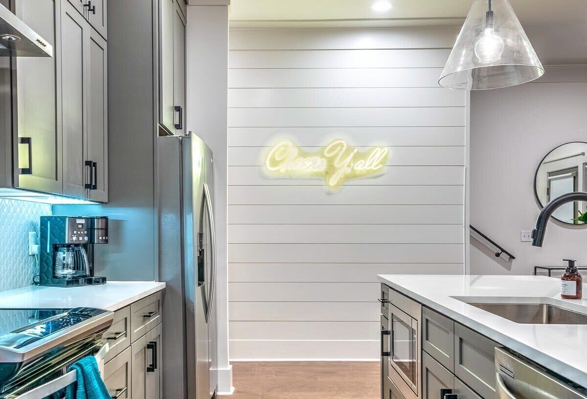 A modern kitchen with a neon sign, stainless steel appliances, and a pendant light.