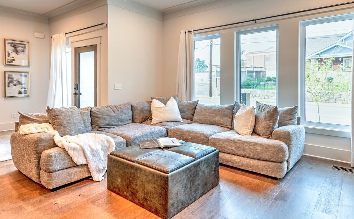 A modern living room with a sectional sofa, a coffee table, and large windows offering a view of the outside.