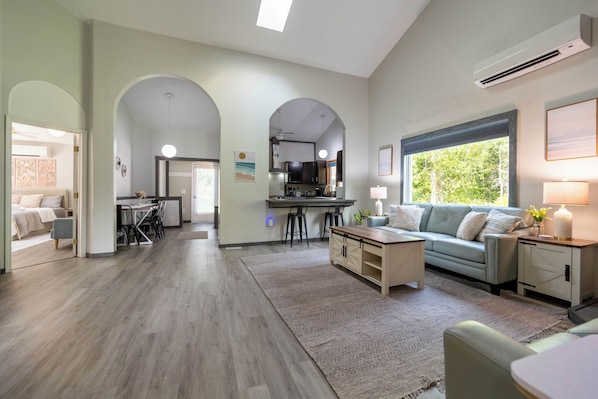 A modern living room with a sofa, coffee table, and a dining area with a kitchen in the background. - Serene "Sol Retreat" by the Shores of Lake Huron and Mackinac Island (Cheboygan)