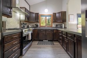A kitchen with dark wooden cabinets, stainless steel appliances, and a large window providing natural light. - Serene "Sol Retreat" by the Shores of Lake Huron and Mackinac Island (Cheboygan)