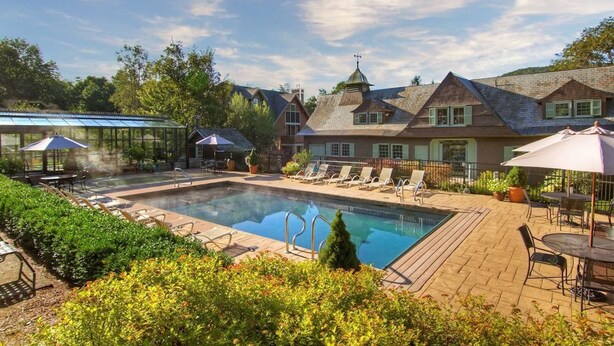 A swimming pool with lounge chairs and umbrellas, surrounded by a brick patio and lush greenery.